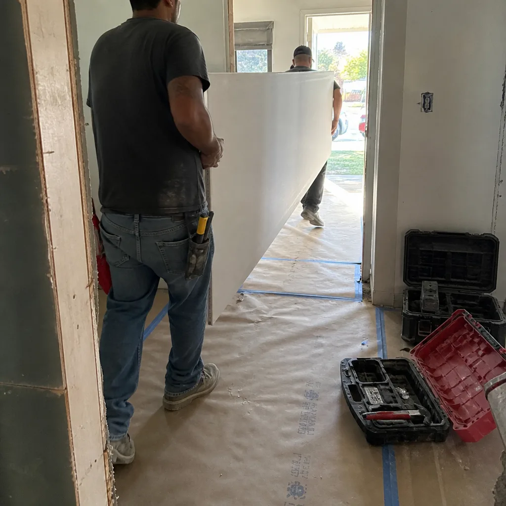 Two construction contractors carrying a drywall panel for a home renovation project